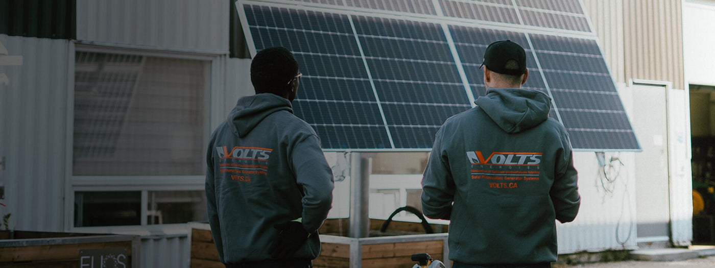 Volts Energies technician installing solar panels on a commercial warehouse rooftop with service trucks parked below
