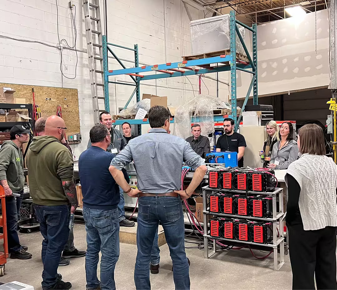 Group of Volts Energies dealers and staff gathered around a live lithium battery bank demonstration in the warehouse